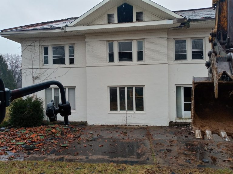 Excavator bucket and grapple at a white building