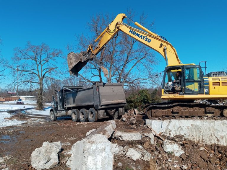 Excavator loading demolition debris into a dump truck