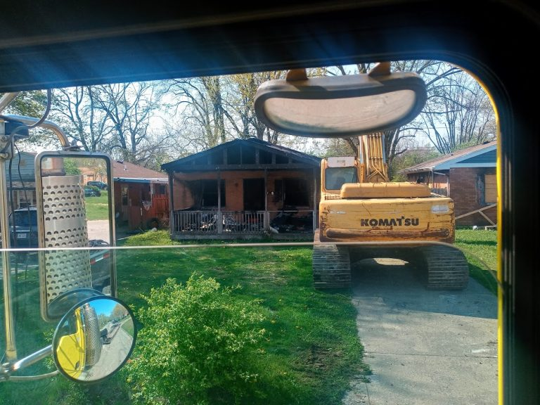 Excavator parked in front of a fire-damaged house