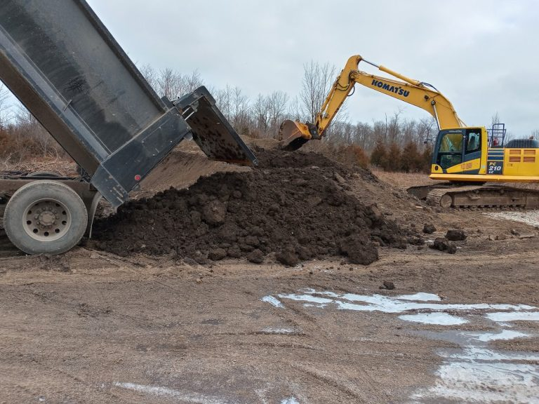 Dump truck unloading soil beside an excavator