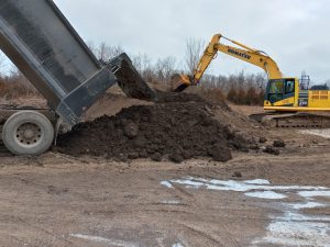 Dump truck unloading material beside an excavator