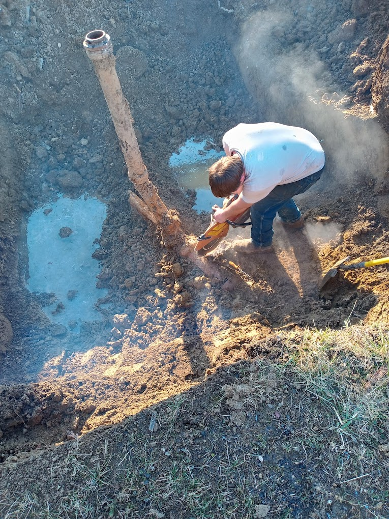 Worker cutting a pipe in an excavated trench